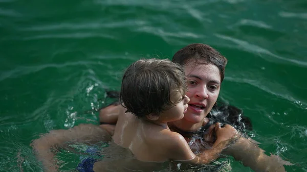 小男孩一边游泳一边抱着妈妈的身体 妈妈和不会游泳的幼儿一起游泳 妈妈在帮孩子父母支助 — 图库照片