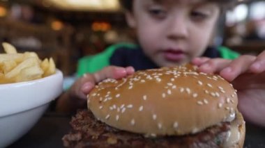 Hamburger yiyen mutlu çocuk. Çocuk hamburgerden bir ısırık alıyor.