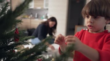 Noel ağacını süsleyen küçük bir çocuk. Yakından bakan çocuk top süslemesi yapıyor