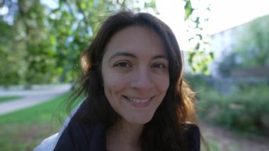 Parkta dikilmiş, 30 'lu yaşlarında gülümseyen bir kadının portresi. Sıradan bir kadın.