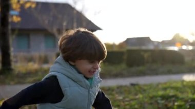 Kaygısız küçük bir çocuk gün batımında parkta koşuyor. Dışarıda koşuşturan mutlu beyaz erkek çocuk. Aktif çocukluk yaşam tarzı gelişimi