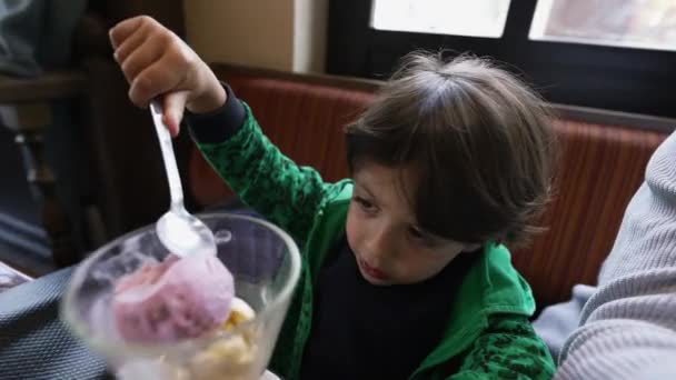 小さな男の子がレストランに座ってアイスクリームデザートを食べています 子供はおいしいイチゴアイスフードスナックを食べる — ストック動画