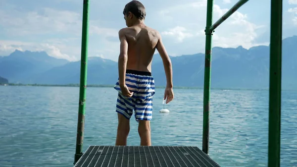 소년은 경치좋은 호숫가 부두에서 서산들을 배경으로 속으로 뛰어들었다 자녀가 여름휴가를 — 스톡 사진