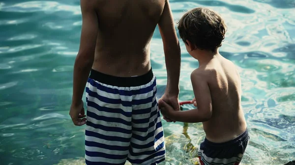 兄は湖の外に立って弟の手を握っていた 水着を着た2人の子供が一緒にぶら下がっている 素晴らしいアウトドアを楽しむ兄弟 — ストック写真