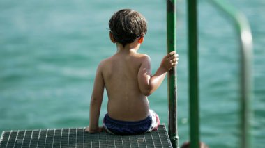Pier Gölü 'nün kenarında oturan küçük bir çocuk. Islak çocuğun sırtı açık havada oturuyordu. Derin düşüncelere dalmış küçük çocuk.