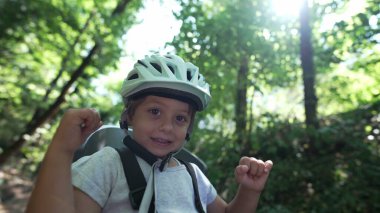 Orman parkında bisiklet kaskı takan mutlu bir çocuk. Bisikletin arkasında oturmuş gülümseyen küçük çocuk hafta sonu aktivitesi yakın plan portresi. Güvenlik ve koruma kavramı