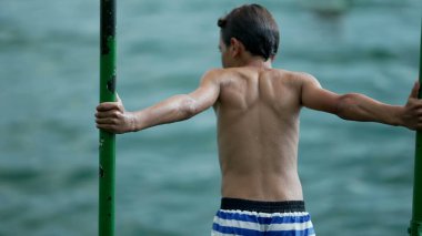 Islak genç çocuğun sırtı rıhtımda duruyor. Düşünceli ergen çocuk yaz tatillerinde açık havada duruyor.