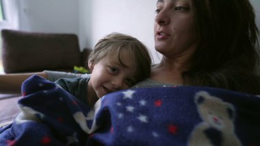 Anne ve çocuk evde battaniyenin altında kanepede oturuyor. Ebeveyn ve çocuk kanepede oynaşıyor.