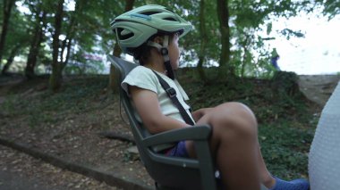 Mother riding bicycle with child in bike seat on green pathway outdoors. Family and weekend activity trip