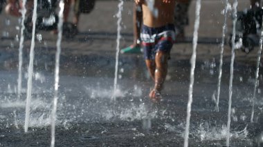 Little boy running toward water jet fountain. Kid having fun at water park during summer day