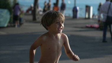 Küçük mutlu bir çocuk yaz tatillerinde açık hava parkında su jetlerine doğru koşuyor.