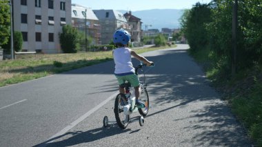 Bisiklet yolu yeşil şehir yolunda bisiklet süren küçük bir çocuk. Miğfer takan çocuk bisikletçi
