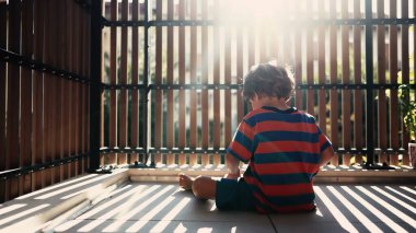 Sabahın köründe bir çocuk alevlerle balkonda oturuyor. Apartman terasında küçük bir çocuk.