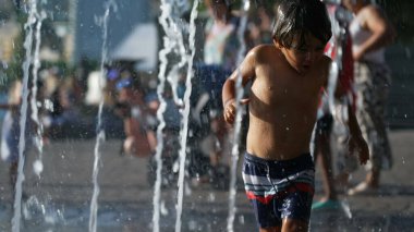 Little boy running toward water jet fountain. Kid having fun at water park during summer day
