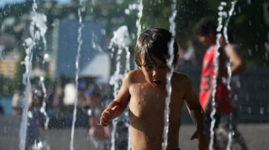 Little boy running toward water jet fountain. Kid having fun at water park during summer day