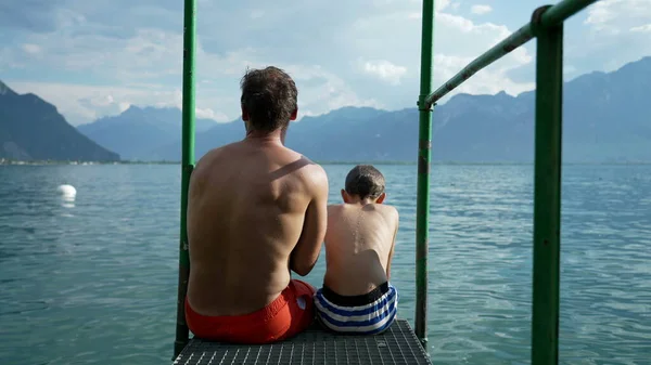 Father Son Sitting Lake Pier Together Overlooking Swiss Mountains Lake — 스톡 사진