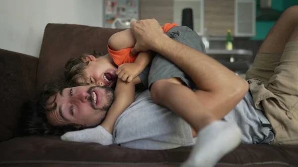 快乐的父亲抱着孩子躺在家里沙发上 真正真实的生活爸爸和孩子在家里的关系 — 图库照片