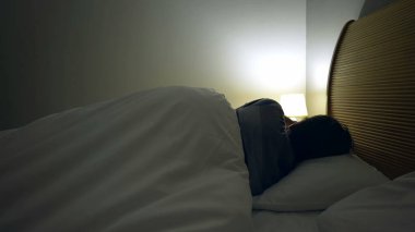 Adam uzun bir günün ardından dinlenmek için yatağa uzandı. Yatak örtüsünün altında uyuyan yatağın başucundaki lambayı kapatır.