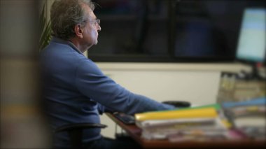 Candid senior man working at night in front of computer screen. One male caucasian older person browsing internet online in work desk