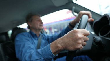 Close up hands holding steering driving in city. One senior male caucasian driver inside moving vehicle