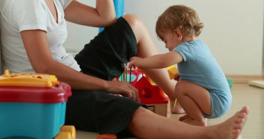 Candid mother with one year old baby child relationship. Real life infant boy playing with toys with mom