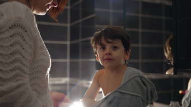 Candid small boy covered with towel sitting in bathroom sink after bath