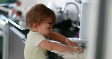 Child playing with flour at kitchen. Baby infant messy hands cooking at kitchen