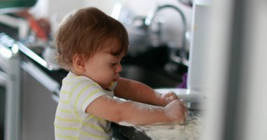 Child playing with flour at kitchen. Baby infant messy hands cooking at kitchen