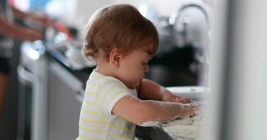 Child playing with flour at kitchen. Baby infant messy hands cooking at kitchen