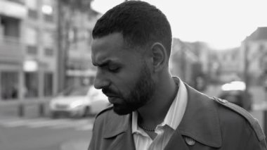 Düşünceli bir Ortadoğu erkeği caddenin dışında duruyor. Düşünceli bir ifadeye sahip bir Arap 'ın monokromatik siyah beyaz dramatik çekimi