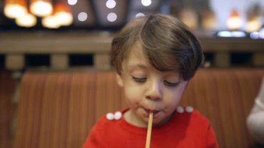 Lokantada oturmuş samandan su içen çocuk. Yakından çekilen çocuk kameraya bakarak içecek içer. Susamış küçük bir çocuk