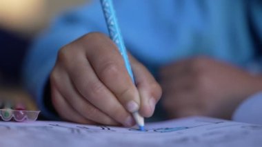 Kağıda mavi renkli kalemle çocuk eli çiziyor. Çocuk Makro 'yu yakına çekiyor. Yaratıcı çocukluk gelişimi