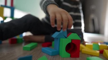 Çocuk eli yerde oturan yapı taşlarıyla oynuyor. Küçük bir çocuk renkli inşaat bloğuyla oynuyor.