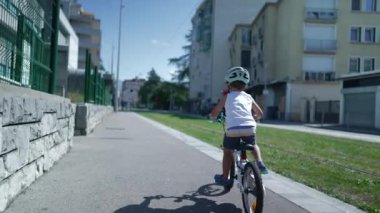 Çocuk şehir caddesinde bisiklet sürüyor. Bisikletli bir çocuğun arka koltuğu kaldırımda bisiklet sürüyor.