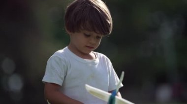 Çocuk parkta planör topluyor ve havaya fırlatıyor. Küçük bir çocuk güneşli bir günde dışarıda uçak oyuncağıyla oynuyor.