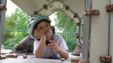 Düşüncelere dalmış çocuk oyun alanında elleri çenesinde kask takarak kaybolmuş. Düşünceli çocuk rüya görüyor