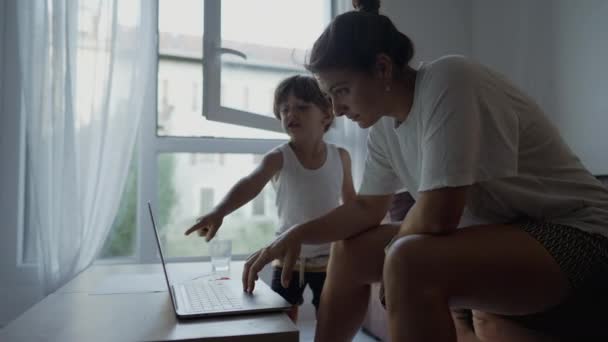 自宅のノートパソコンの画面の前で母親と子供 息子がコンピューターを指してる 若い男の子とインターネットを閲覧することができます — ストック動画