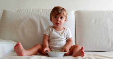 Cute baby with plate on sofa. Adorable sweet infant toddler boy on home couch