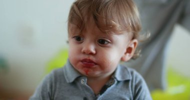 Cute one year old baby eating food. Portrait infant toddler with mouth full chewing