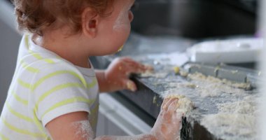 Messy baby child covered with flour at kitchen. Infant one year old toddler boy playing at kitchen