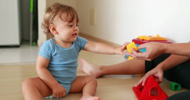 Mother showing baby to play with puzzle toys at home indoors