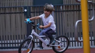 Aktif bir bisikletçi çocuk oyun parkının dışında bisiklet sürüyor. Bisiklete binen küçük çocuk