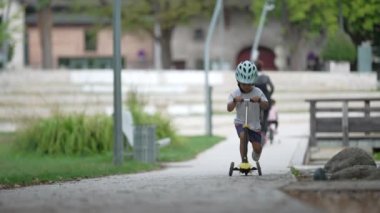 Parkta scooter kullanan eğlenceli bir çocuk. Koruyucu kask takan çocuk dışarıda geziyor.