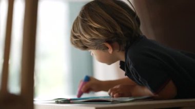 Küçük bir çocuk evde okul aktivitesi yapıyor. Çocukluk gelişimi kavramı. Kalemle resim yapan samimi çocuk.