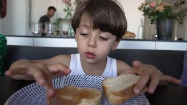 Kahvaltı masasında reçelli ekmek yiyen küçük bir çocuk. Çocuksu bir yaşam tarzı. Aile karbonhidrat tadı alıyor.
