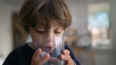 Susamış bir çocuk içeride bir bardak su içiyor. Su içen küçük çocuk.