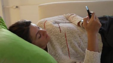 Kanepede uzanmış telefonu kullanan kişi. Akıllı telefon aygıtında internette gezinen kadın