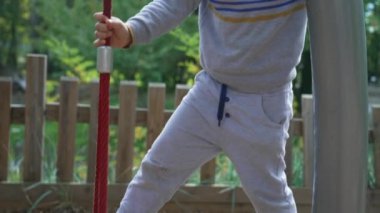 Oyuncu küçük çocuk oyun alanındaki ipi dengede tutuyor. Çocuk spor yapıyor ve parkta oynuyor. Çocuk aktif.