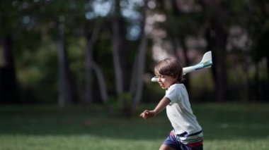 Küçük çocuk parkta uçak oyuncağıyla koşuyor. Kaygısız Çocuk uçak planörü fırlatıyor ve eğleniyor. Neşeli çocuk güneşli bir günde köpük uçak fırlatıyor.