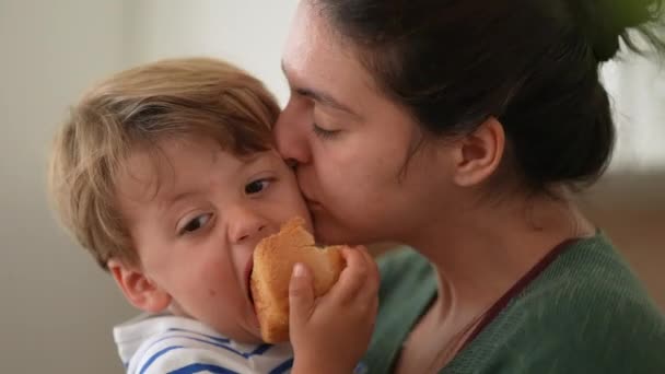 有爱心的母亲一边吃面包一边亲小男孩的脸 父母幸福的概念 妈妈拥抱和拥抱孩子 罐头食品生活方式 — 图库视频影像
